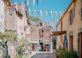 Rue européenne étroite, drapeaux colorés flottant au-dessus des têtes. Bâtiments en pierre, boutiques et piétons.