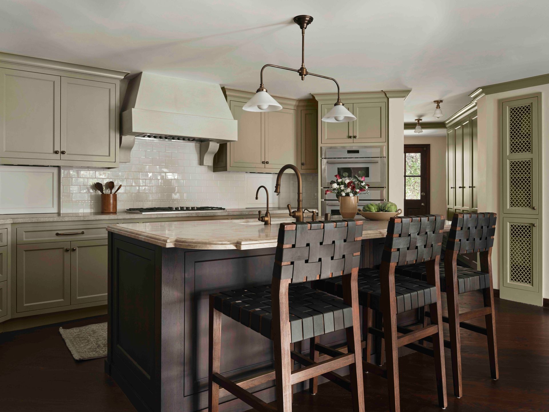 Modern kitchen with an island, dark wooden stools, light gray cabinets, a white range hood, and dark hardwood floors.