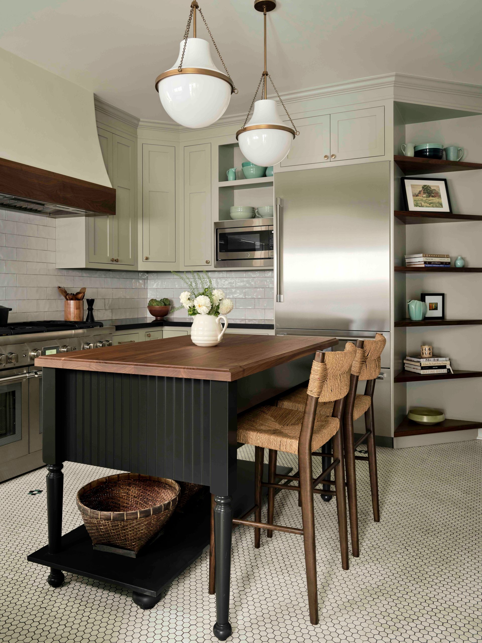 Modern kitchen with a black island, wooden countertop, woven stools, stainless steel fridge, and open corner shelving.