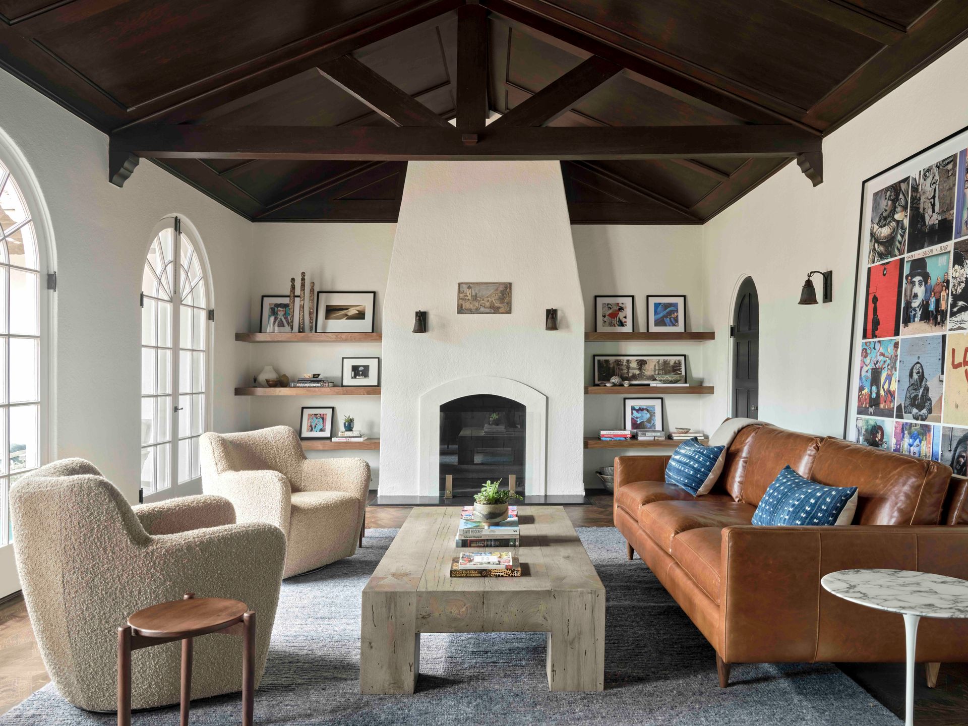A living room with a wood-vaulted ceiling, white fireplace, tan sofa, two textured armchairs, and a wood coffee table.