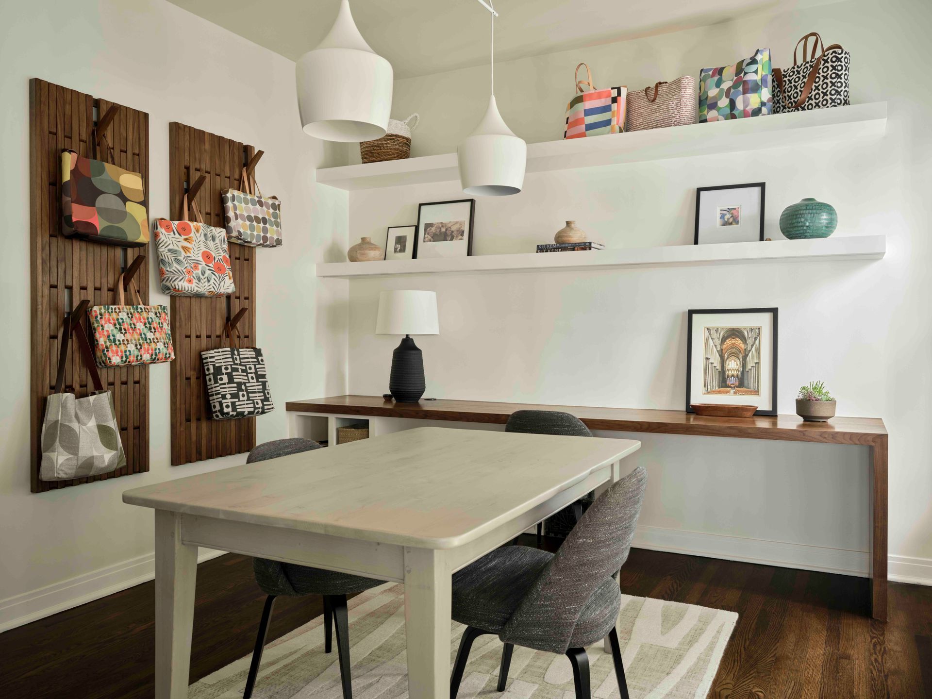 A dining room with a wooden table, chairs, wall-mounted bag racks, floating shelves, and a built-in desk.