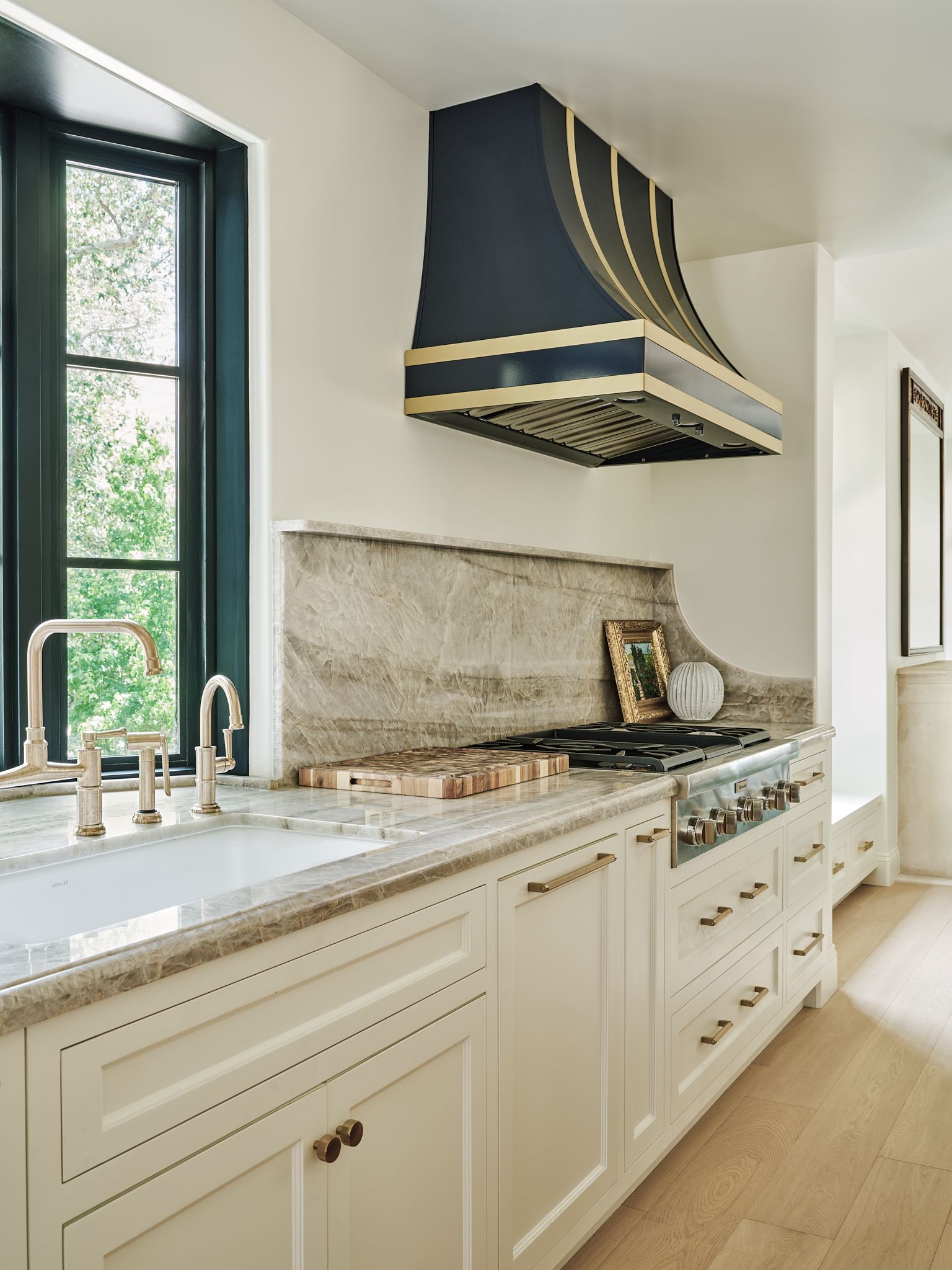 Kitchen with cream cabinets, gas range, white backsplash, and decorative hood.