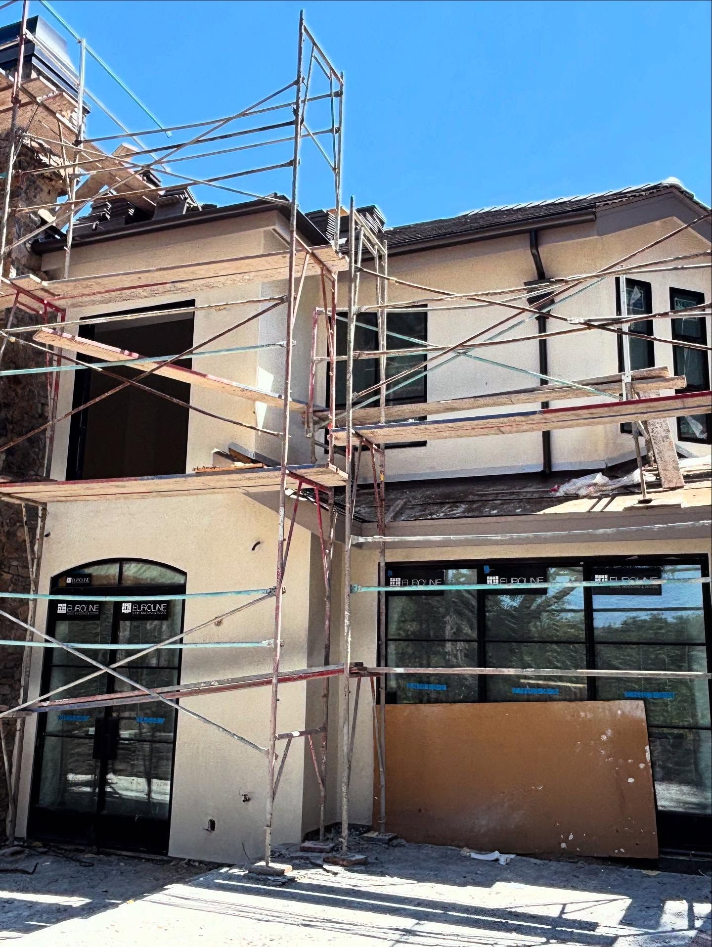 Building under construction with scaffolding against stucco walls and window frames.