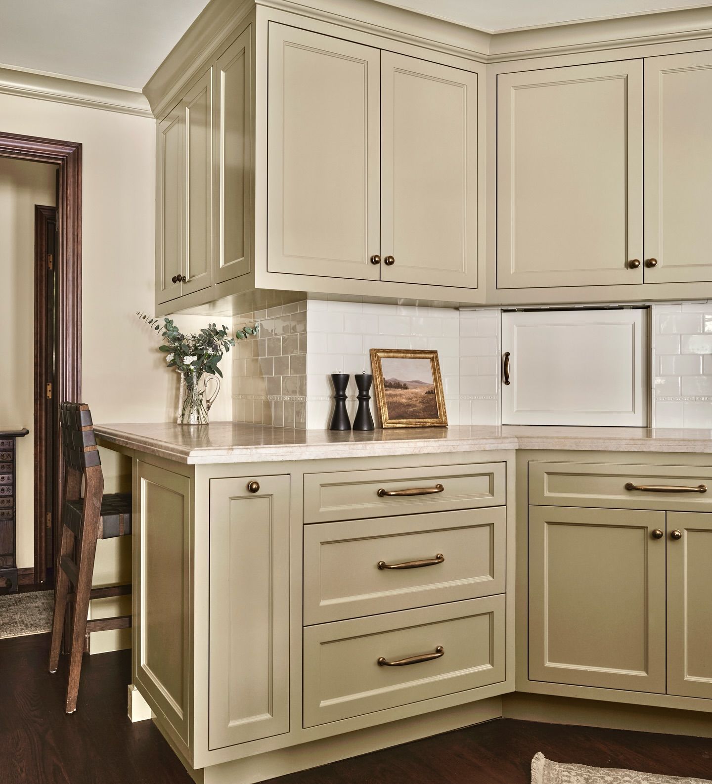 Cream-colored kitchen cabinets with brass hardware, tile backsplash, and dark wooden floors.