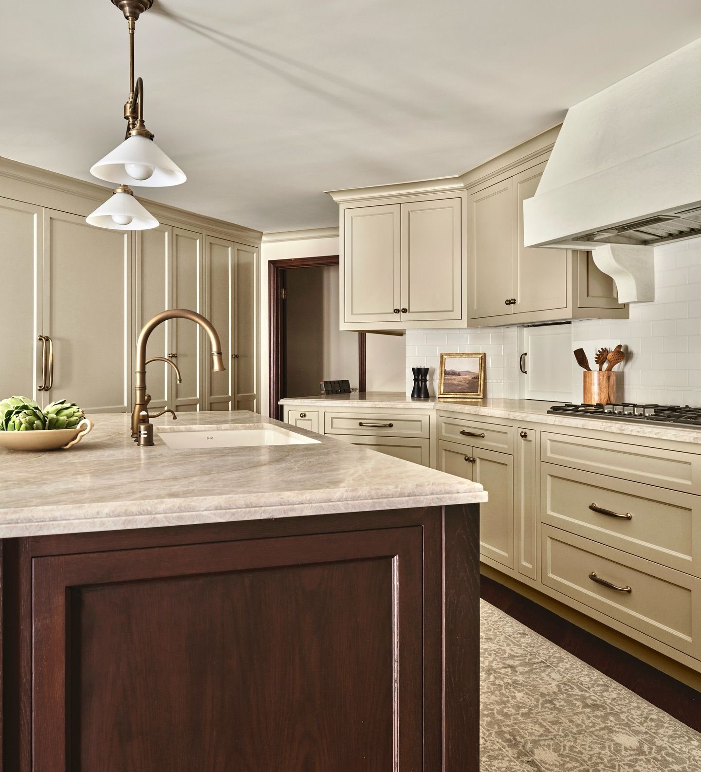Kitchen with cream-colored cabinets, brown island, and brass fixtures. White countertops and a range hood complete the space.