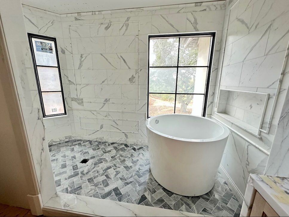 Bathroom with marble tile walls, a round tub, two windows, and patterned floor tile.