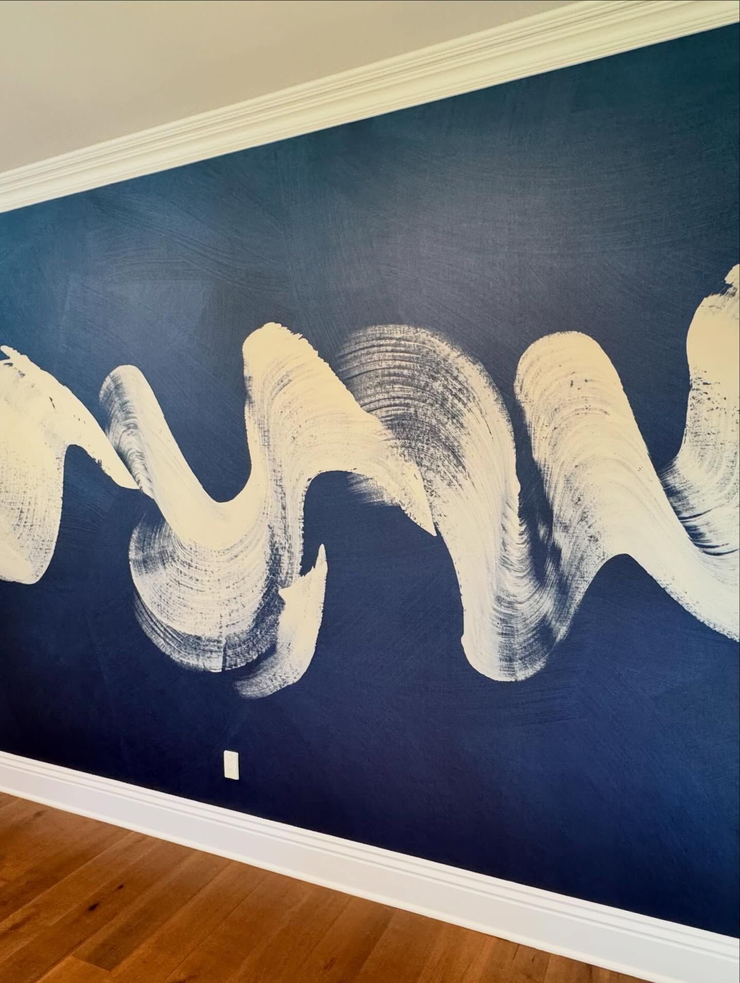 Dark blue wall with a white abstract wave design. Wooden floor and white trim at the top.