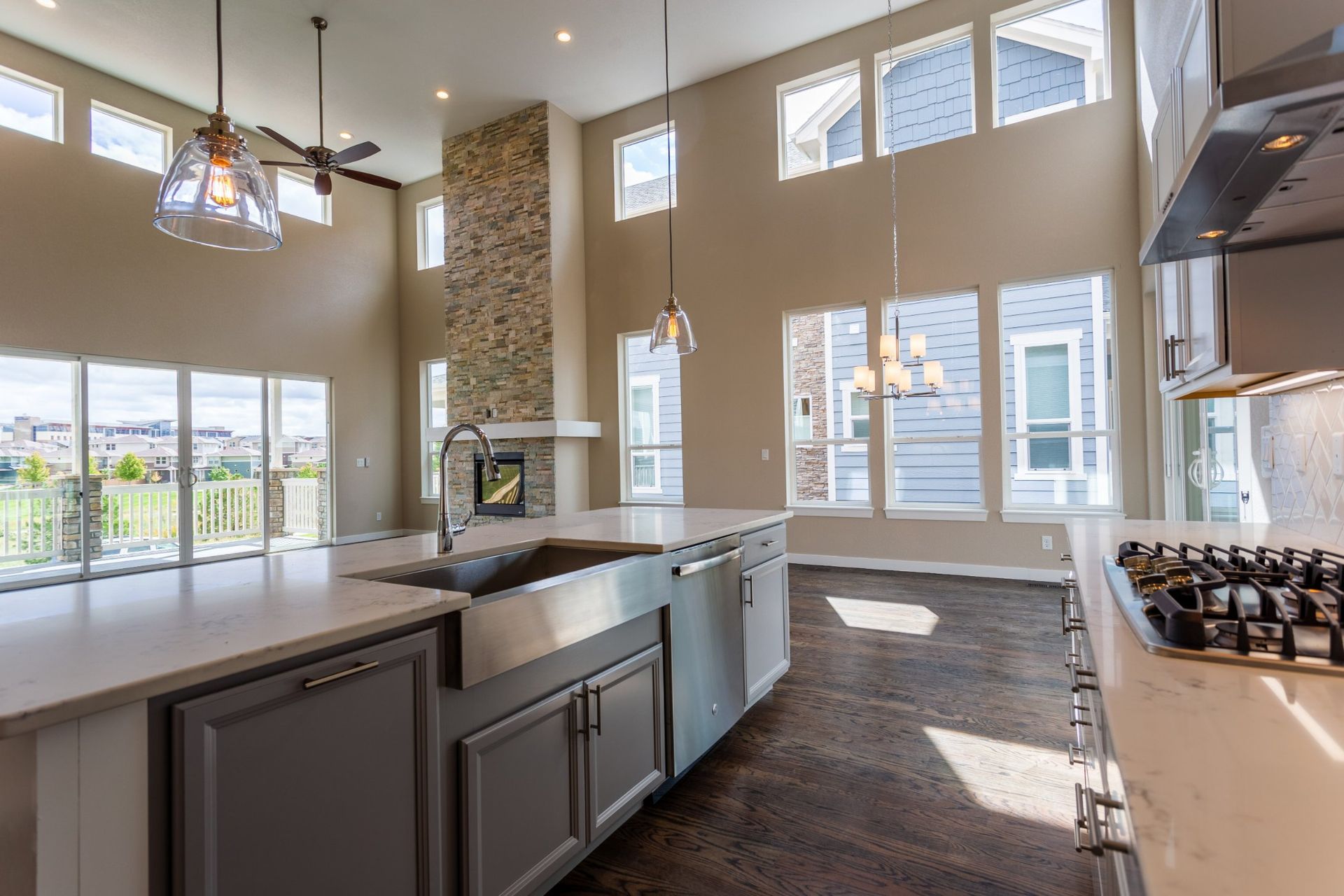 Open-concept kitchen with island, stainless steel sink, and large windows overlooking a green yard and blue sky.