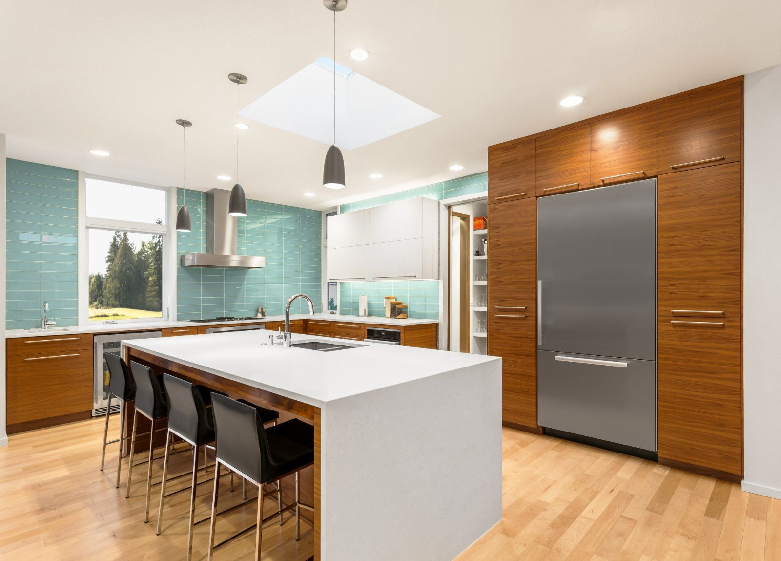 A modern kitchen with wood cabinets, a white island with bar stools, stainless steel refrigerator, and light blue walls.
