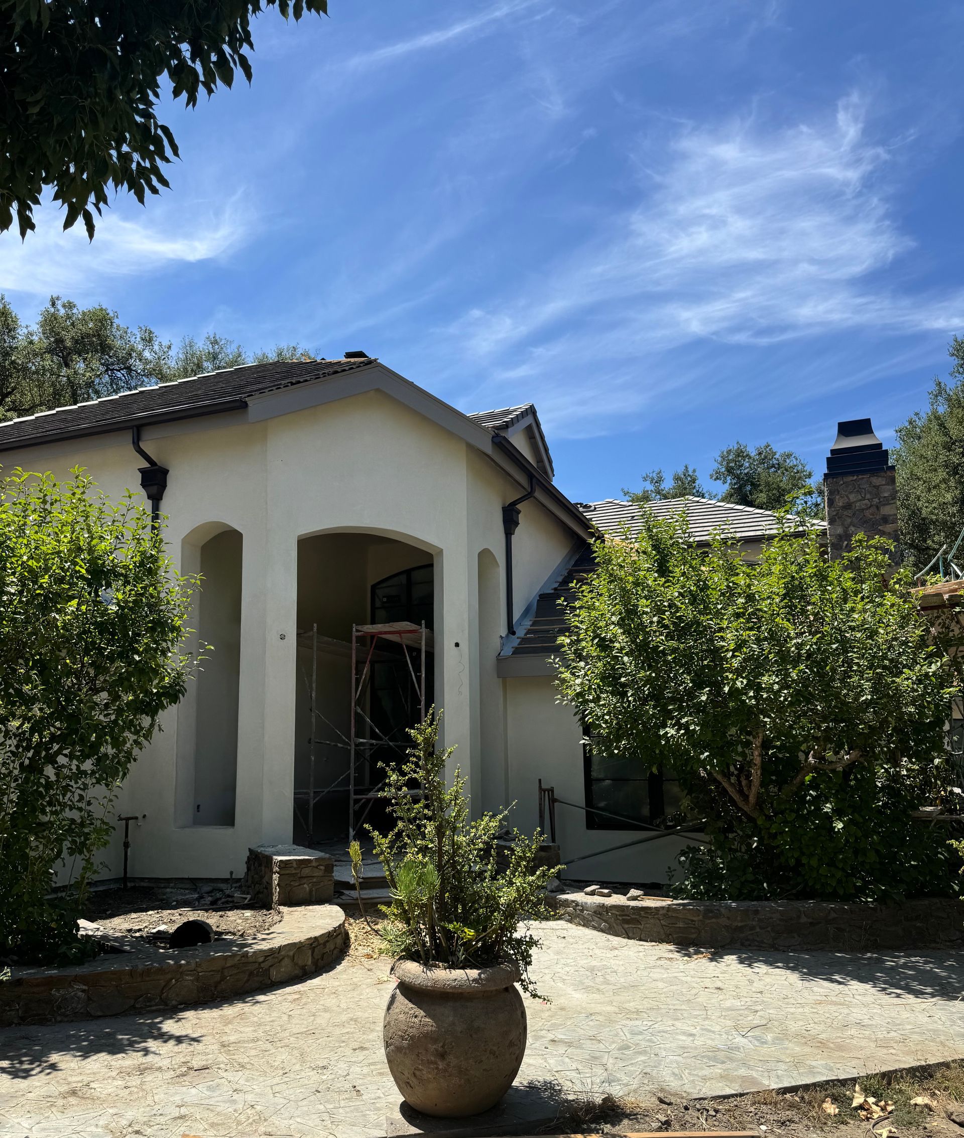 A light-colored stucco home features a recessed entryway, tiled roof, and a stone-lined garden path with potted plants.