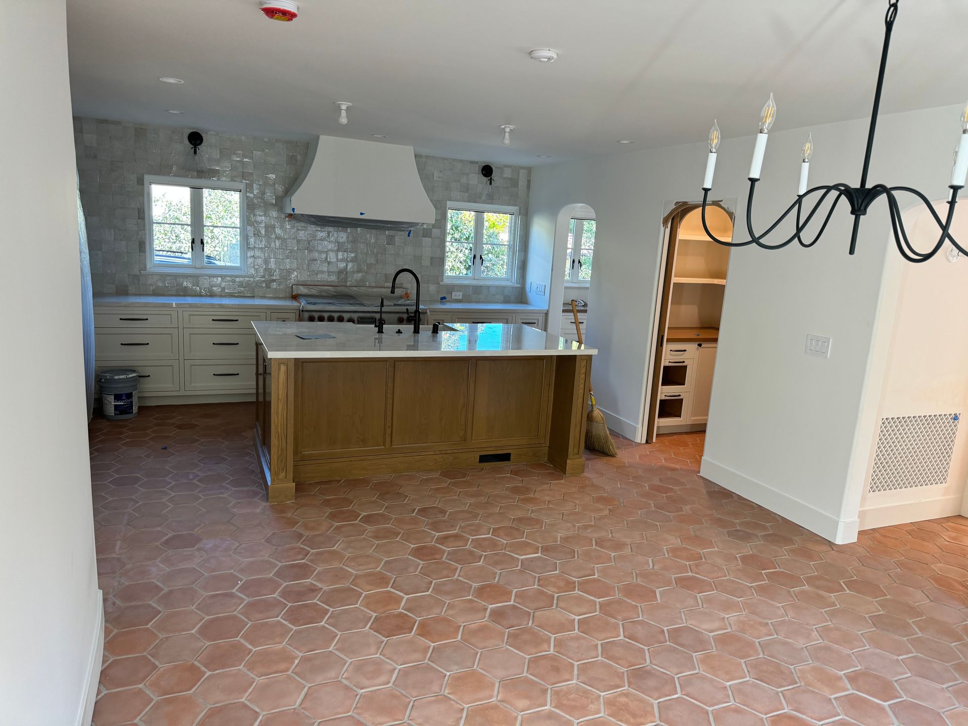 A kitchen with a wood island, white cabinets, white range hood, and light-colored hexagonal tile flooring.