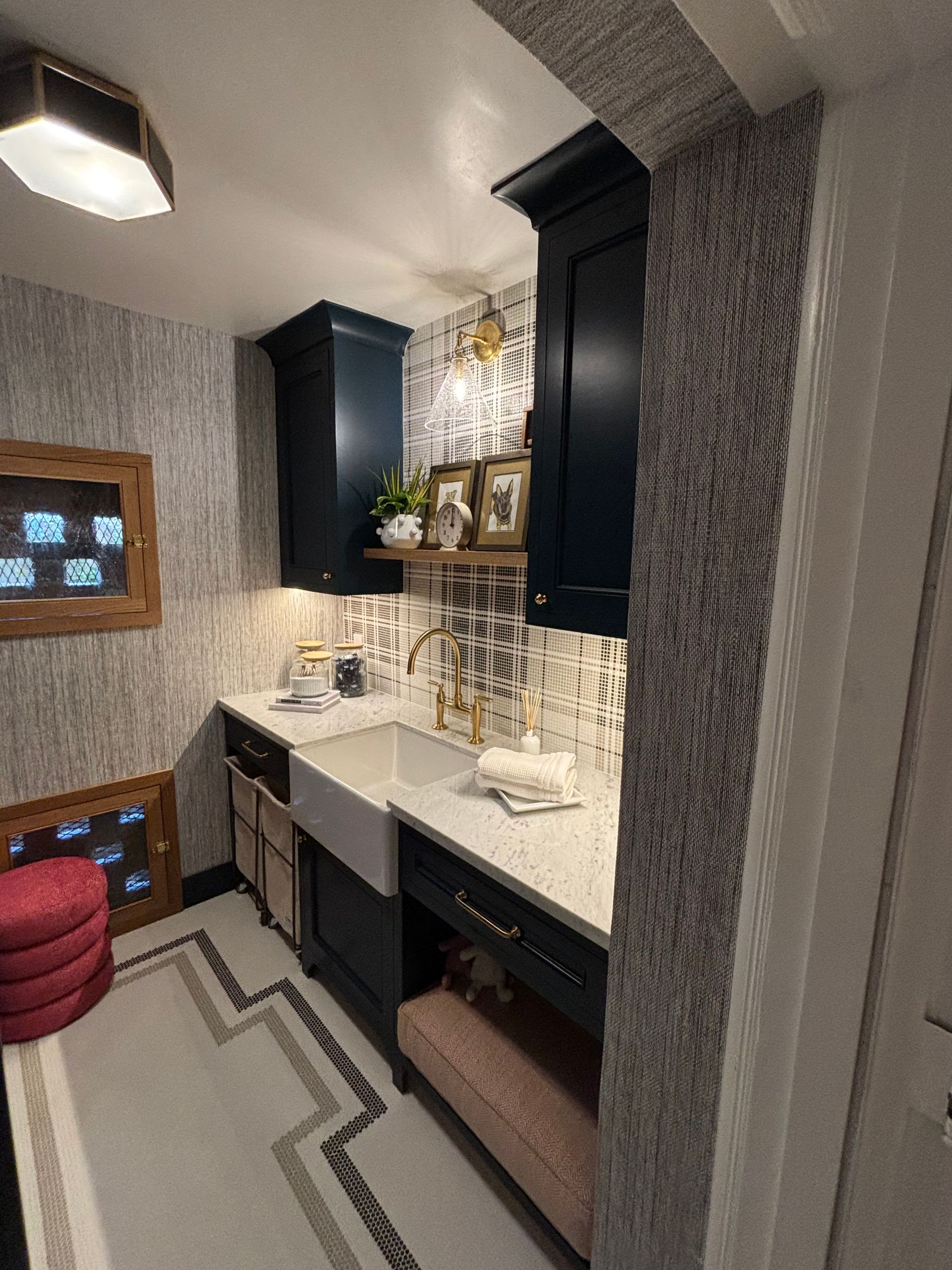 A small laundry room or butler's pantry with navy cabinets, white stone countertops, a farmhouse sink, and patterned paper.