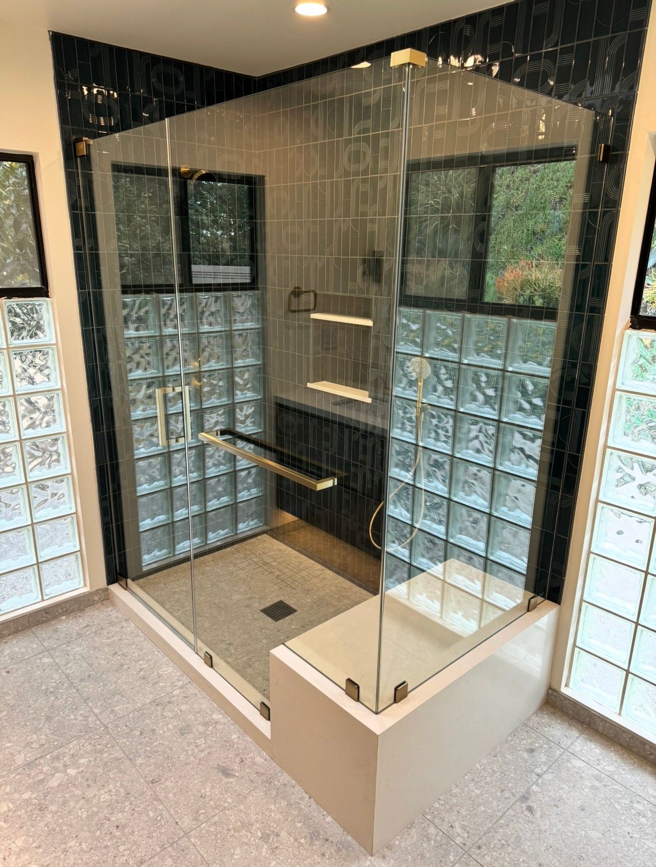 A walk-in shower with glass doors, a stone bench, and interior walls made of clear glass blocks and dark, vertical tile.
