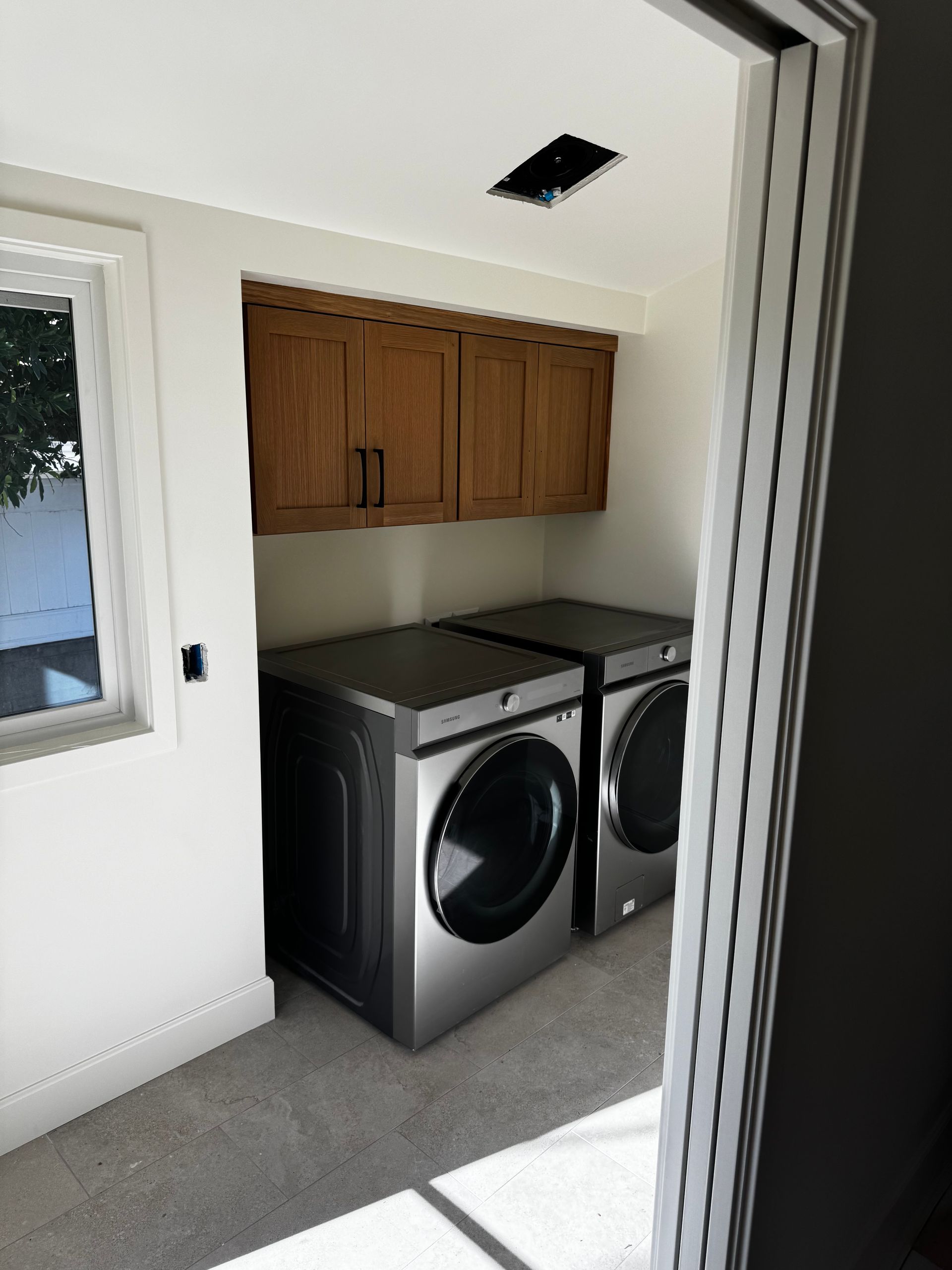 A laundry room featuring two side-by-side silver washer and dryer units with wooden cabinets mounted above.