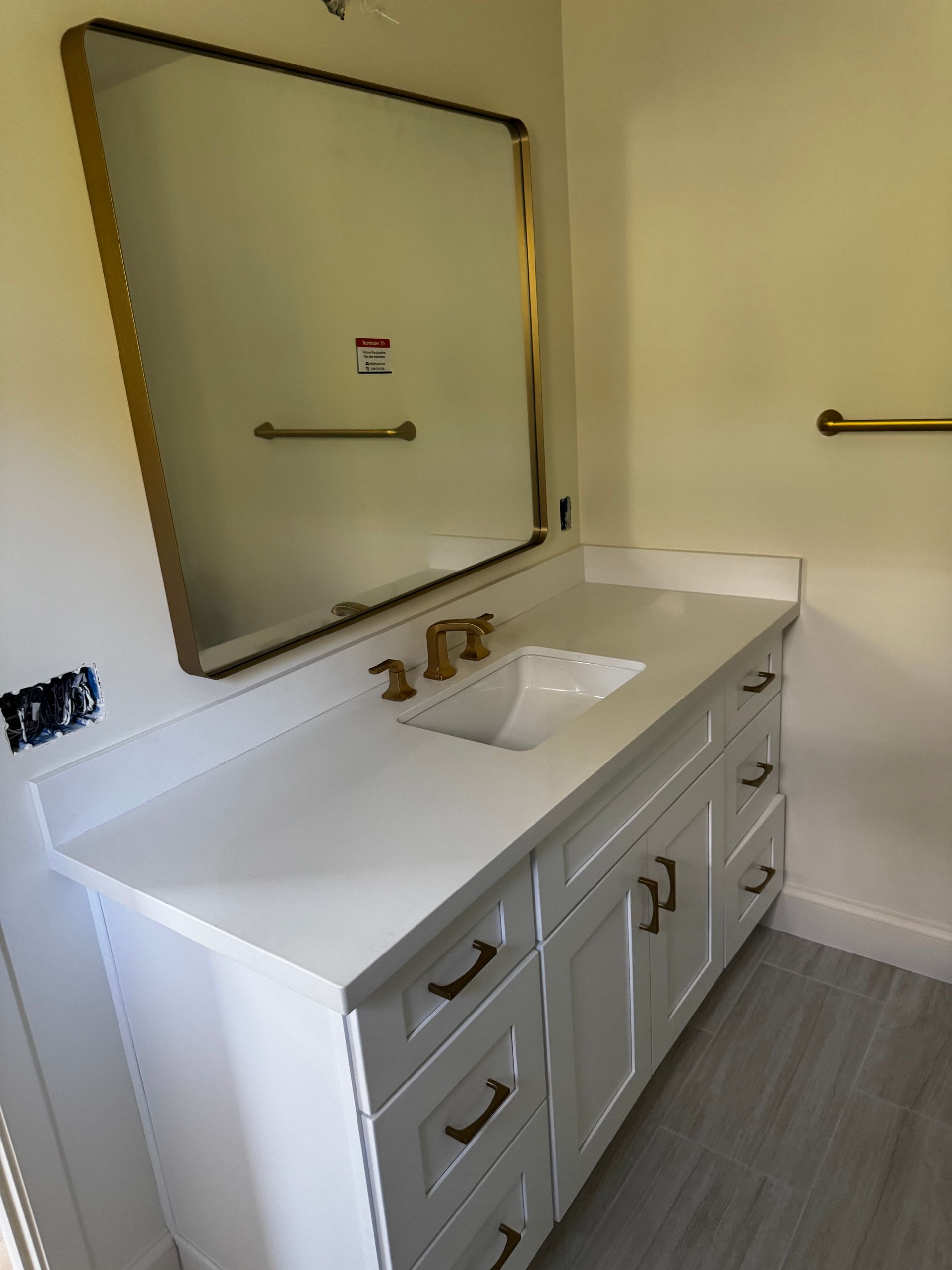 A white bathroom vanity with gold hardware, a rectangular gold-framed mirror, and a matching gold towel bar on the wall.