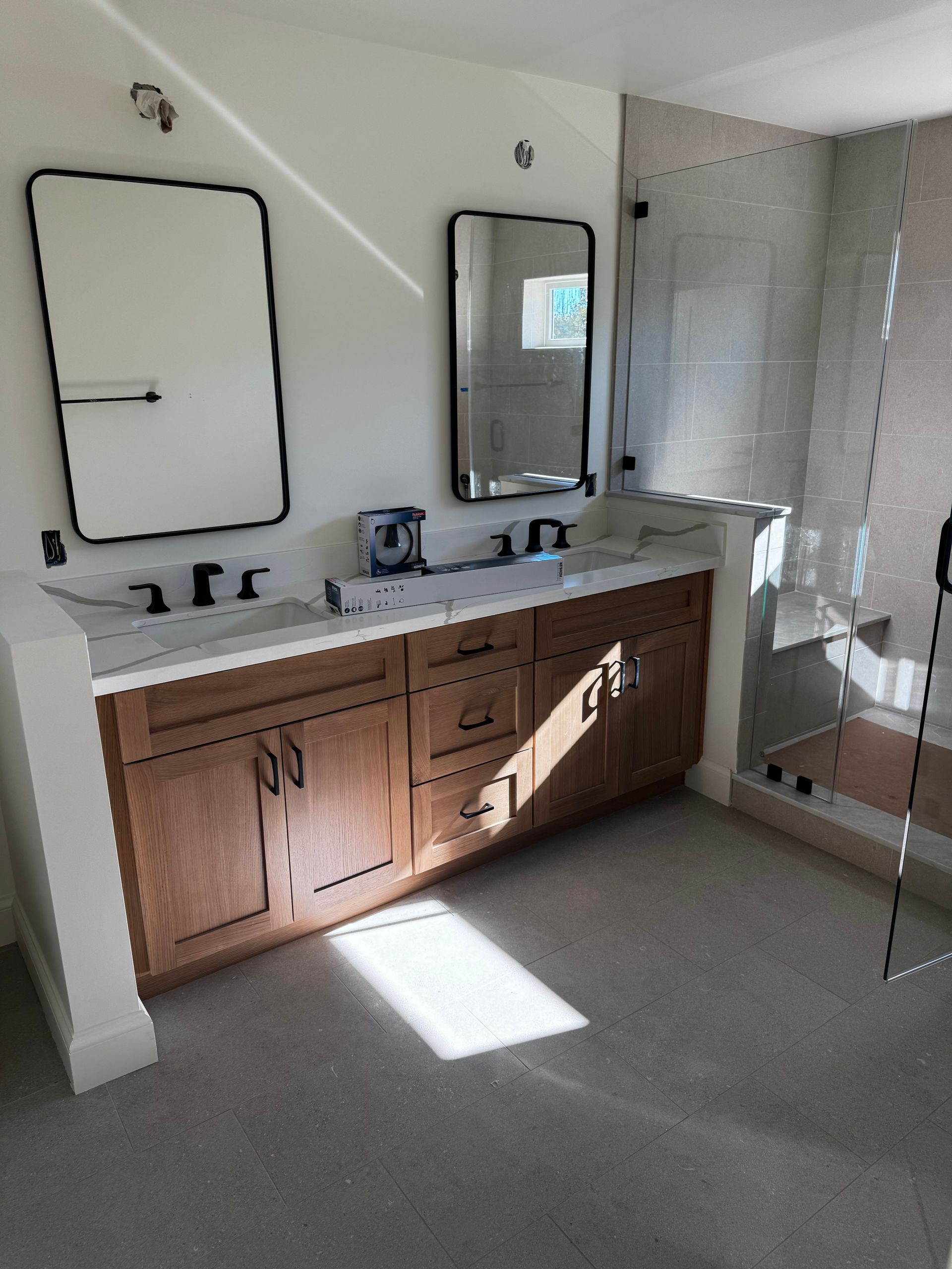 A bathroom vanity with a wood cabinet, white countertop, two rectangular mirrors, and a glass-enclosed shower nearby.
