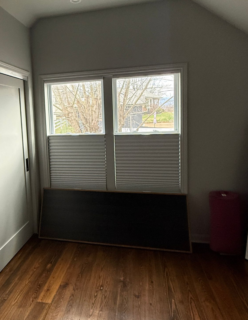 Room with two windows, wood floor, and a large black object leaning against the wall below the windows.