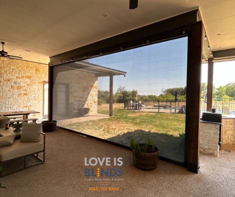 Outdoor patio with a large screen, stone wall, and view of a backyard with a pool.