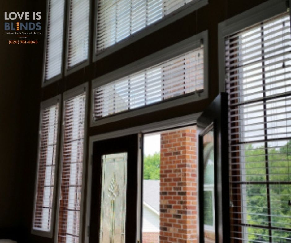 Interior view of large windows with blinds, brick wall, and exterior view of trees.