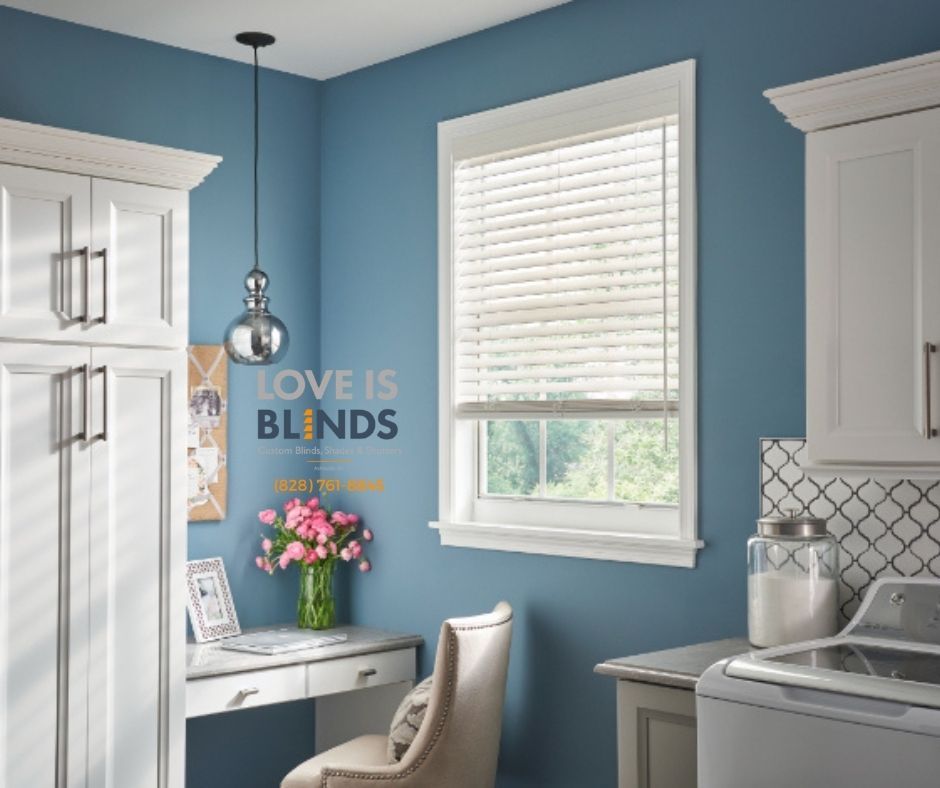 Blue laundry room with white cabinets, desk, and blinds; a vase of flowers sits on the desk.