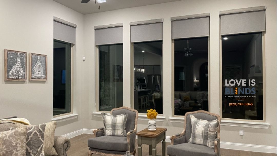 Living room with gray roller shades, two gray armchairs with pillows, and artwork.