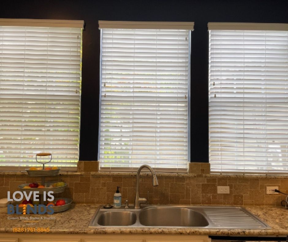 Kitchen with three windows, blinds closed, above a sink and countertop. Beige tile backsplash.