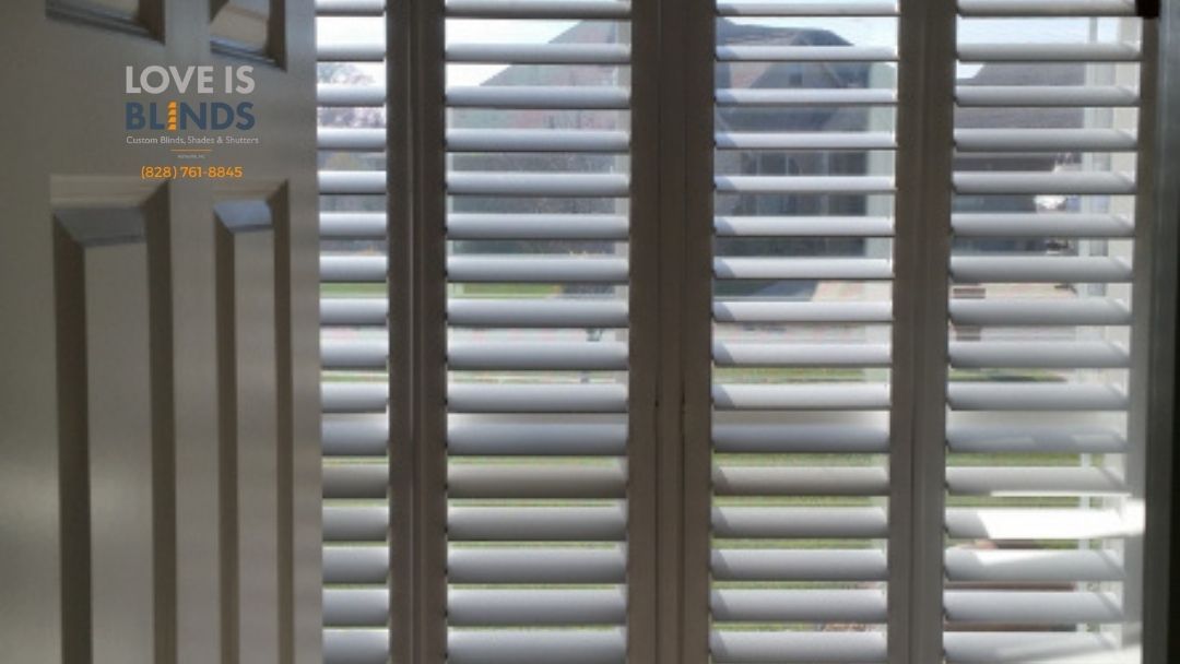 White interior shutters on a window, partially obscuring a view of a building outside.