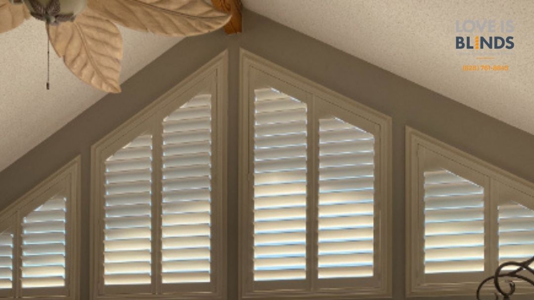 Shutters in a triangular window, beige and white, with sunlight.