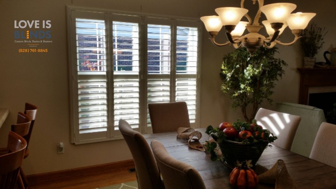 Dining room with table set for a meal, sunlight through window shutters.