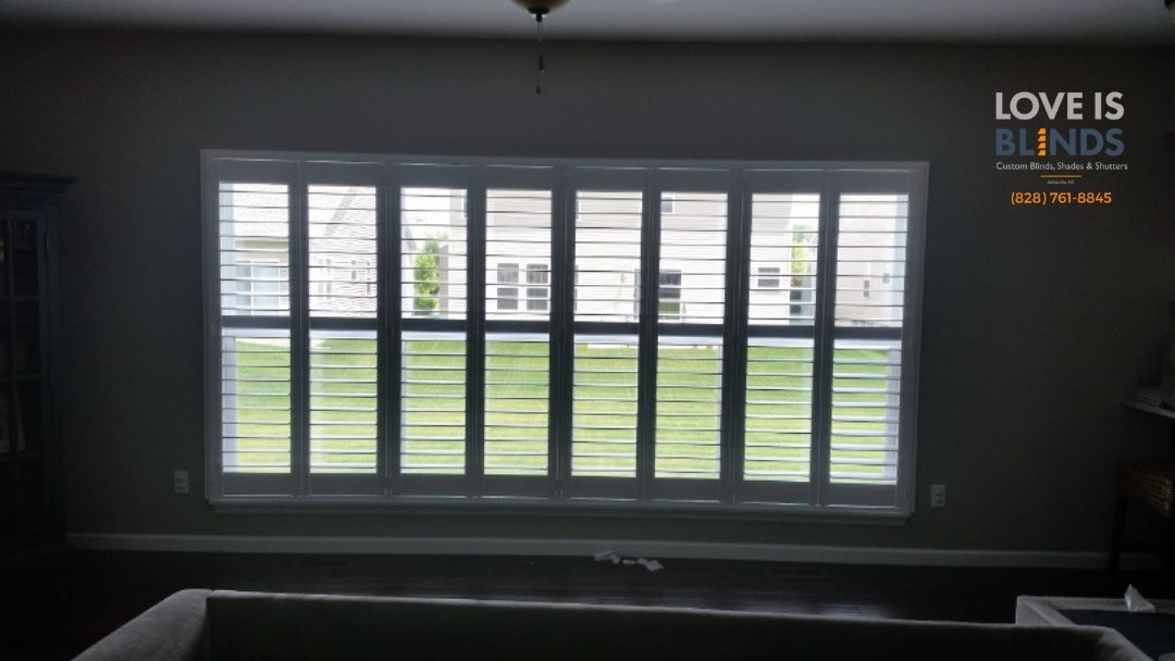 Large window with blinds, interior view. Green outdoor scenery visible. Gray walls.