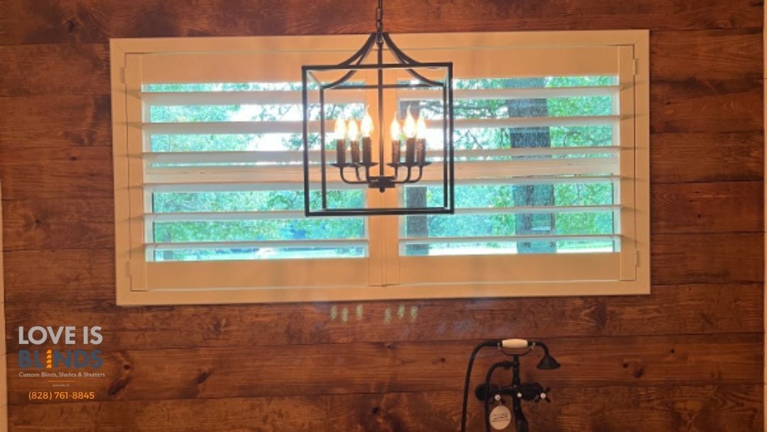 Rustic bathroom with wood paneling, shuttered window, and chandelier.