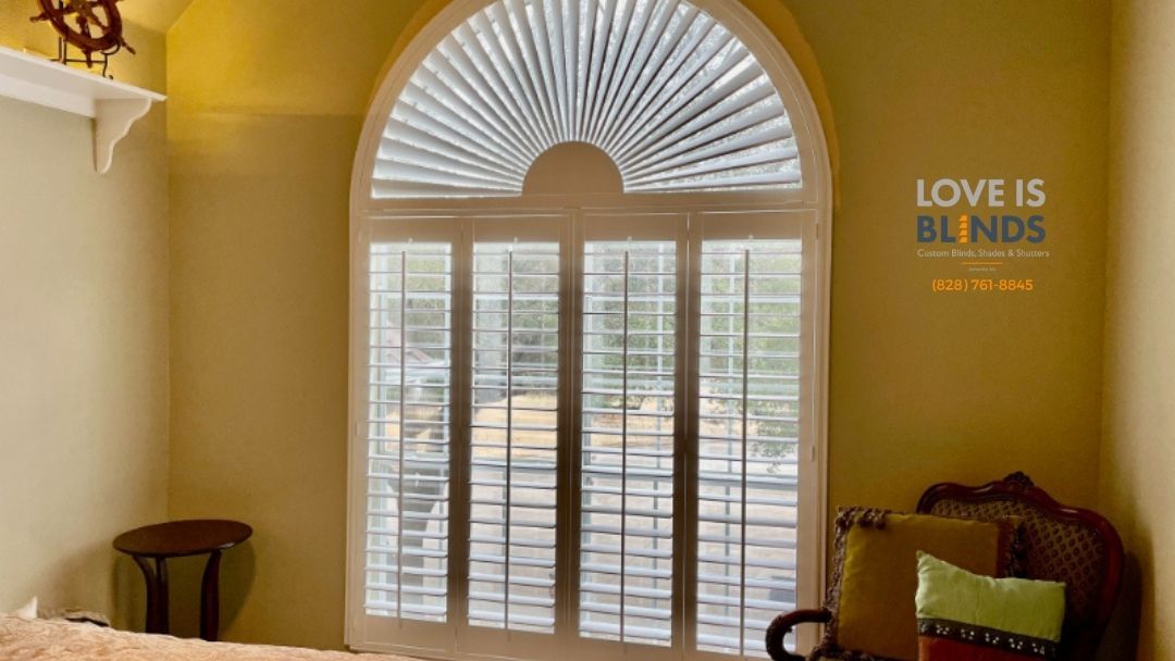 Arched window with white shutters, in a room with yellow walls.