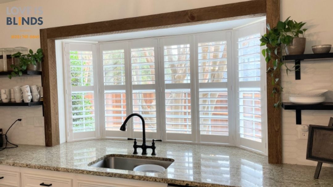 Kitchen window with white shutters, black faucet, granite countertop, and wooden trim.