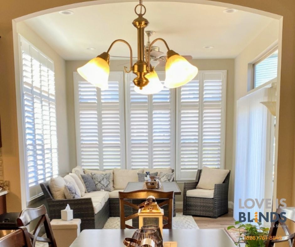 Sunroom with white shutters, sectional sofa, dining table, and chandelier.