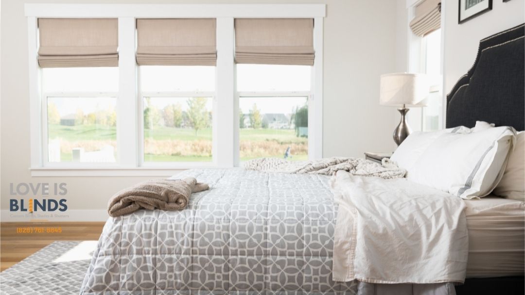 Bedroom with windows, bed, neutral roman shades, soft bedding.