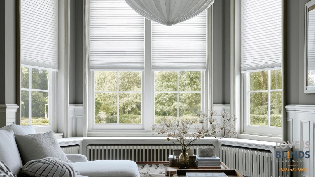 Living room with white honeycomb blinds, white sofa, and windows overlooking greenery.
