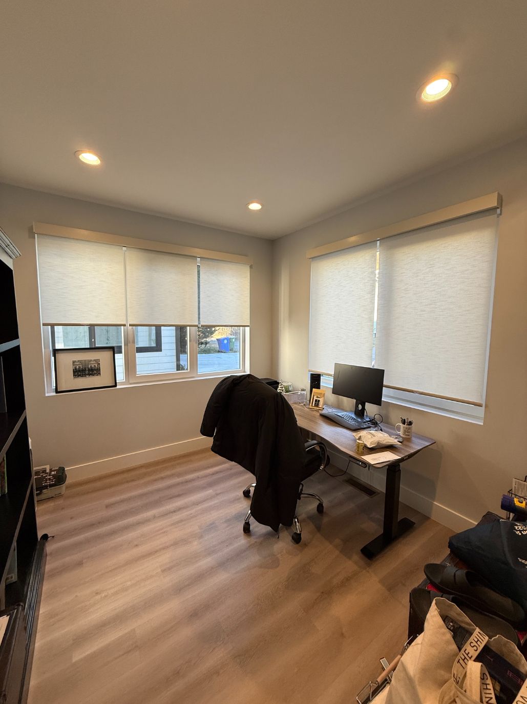 Home office with desk, chair, computer monitor, windows with roller shades, and wood flooring