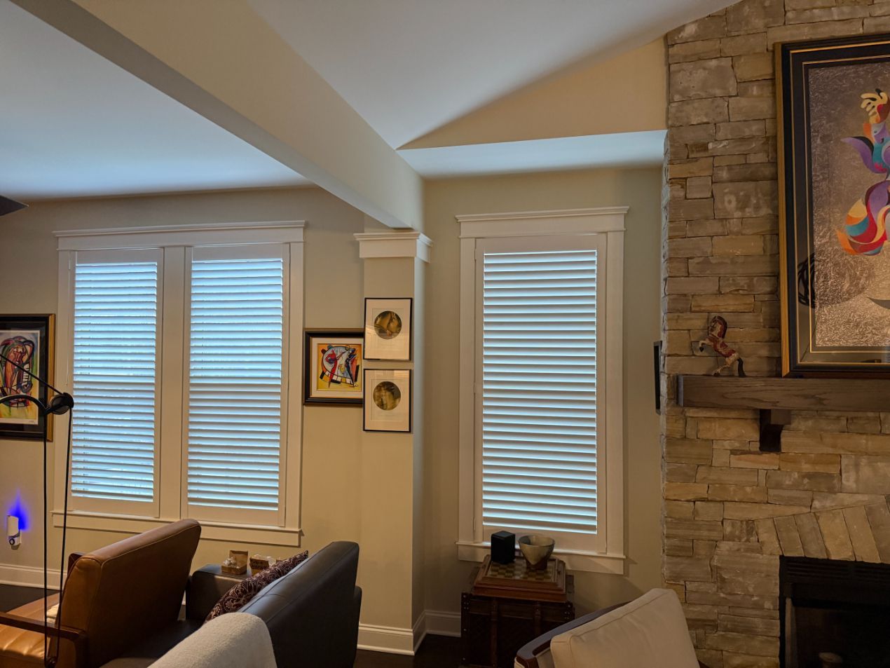 Cozy living room with large windows, stone fireplace, and framed art on the wall