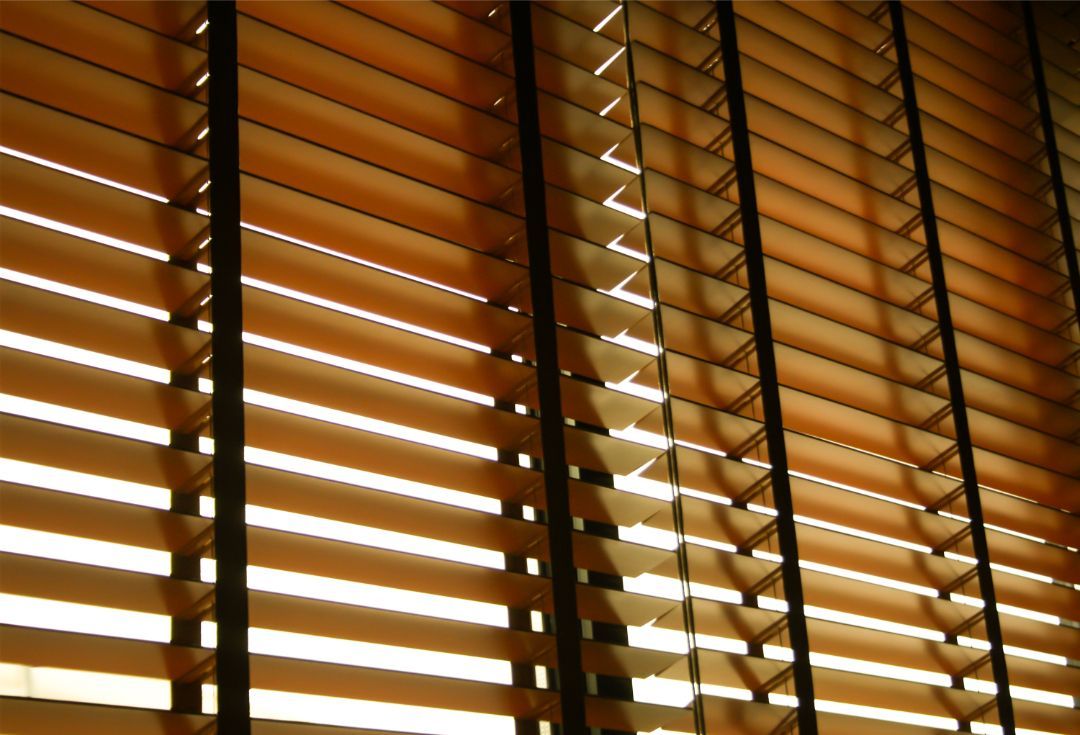 Wooden blinds, closed, casting shadows and allowing some light to filter through.
