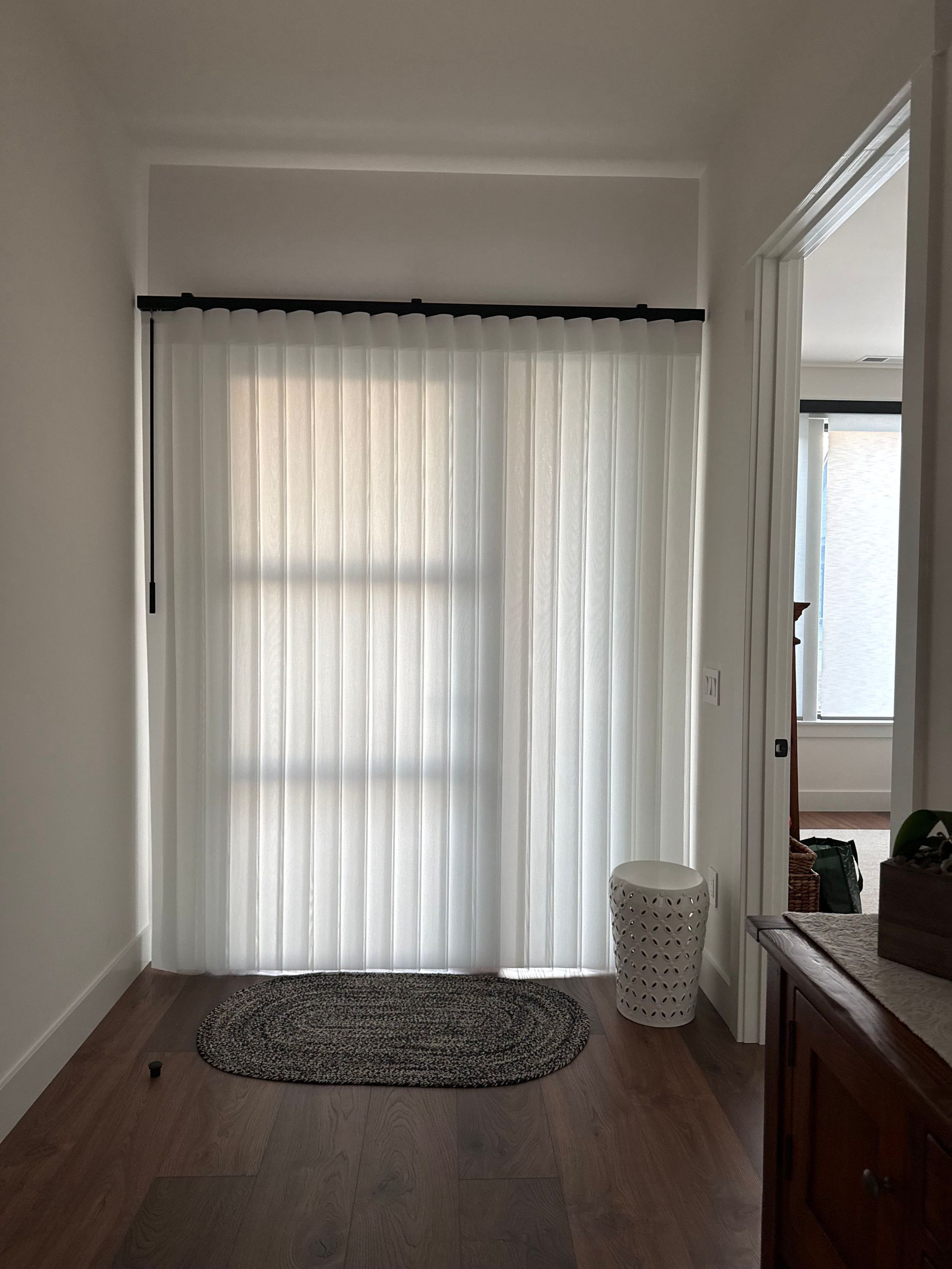 A hallway featuring a floor-to-ceiling white curtain, a patterned oval rug on wood flooring, and a white decorative stool.