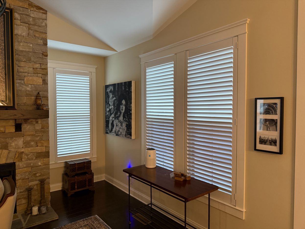 A corner in a living room has two windows with plantation shutters.