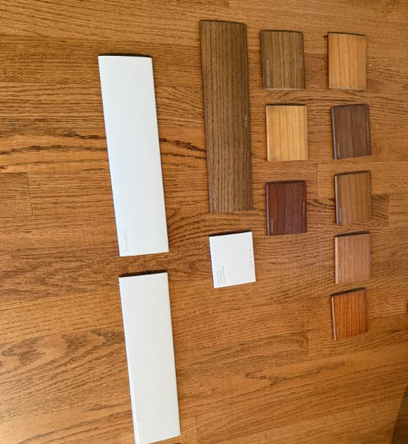 Wood sample boards and color swatches arranged on a wooden floor, including white and brown finishes