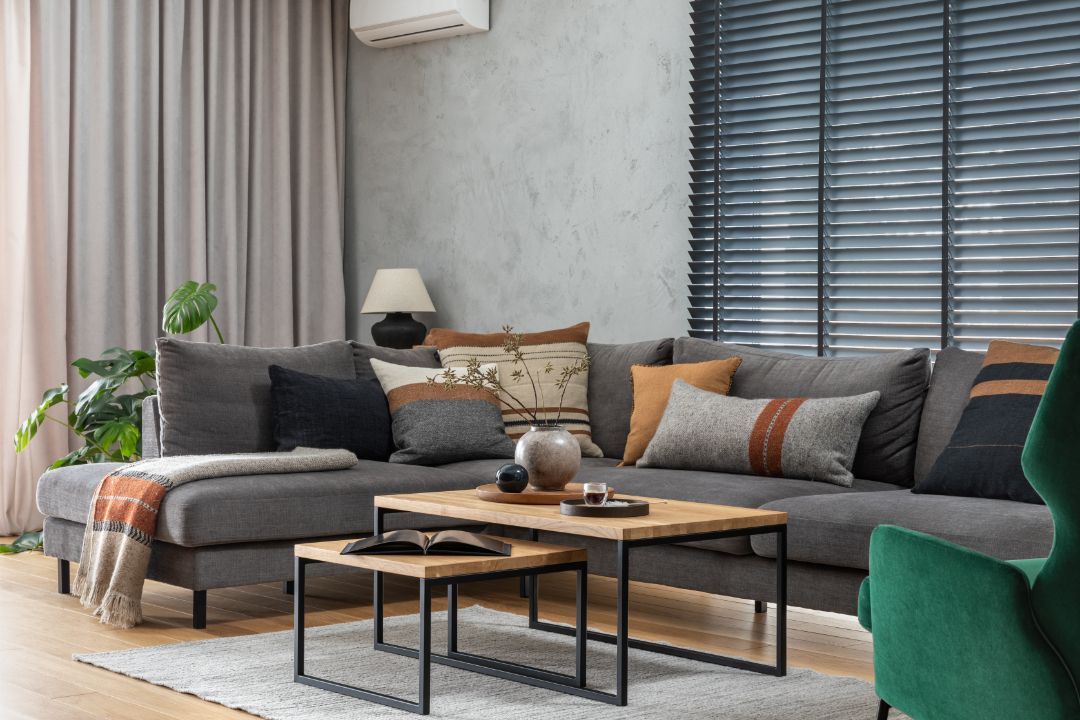 Gray sectional sofa in a living room with various pillows, wooden coffee tables, and a green armchair.