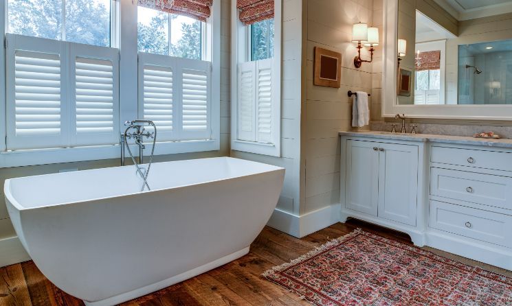 White wood shutters are on the windows in an elegant bathroom. 