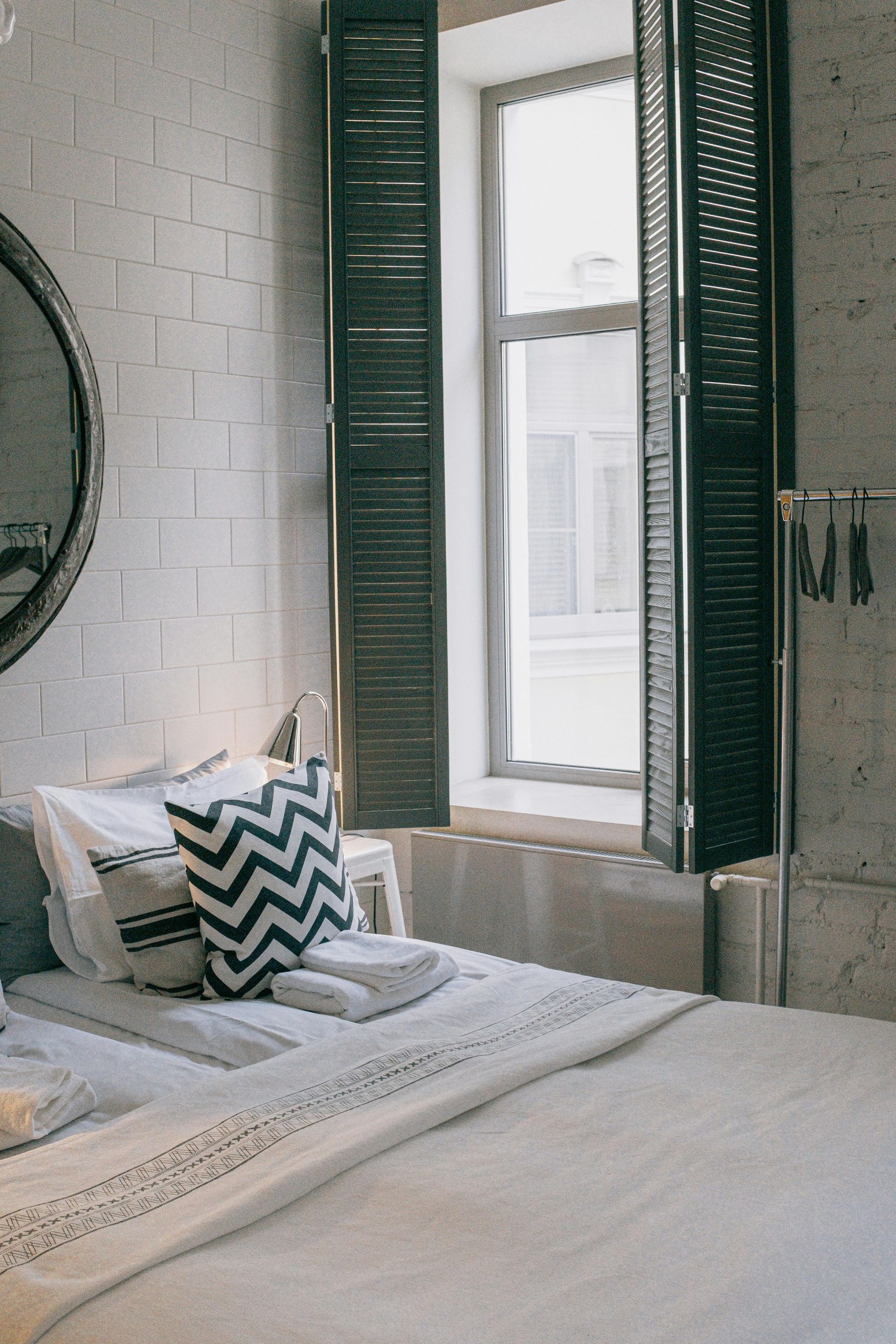 Bedroom with white brick wall, bed with patterned pillows, and window with dark shutters.