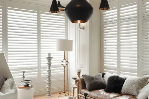 A living room with a couch , chair , lamp and white shutters. Love is Blinds North Carolina