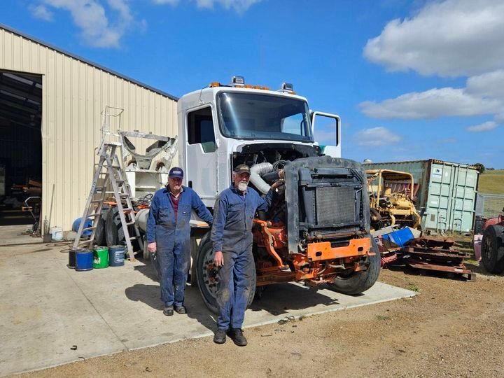 Two men are standing in front of a truck with the hood open.