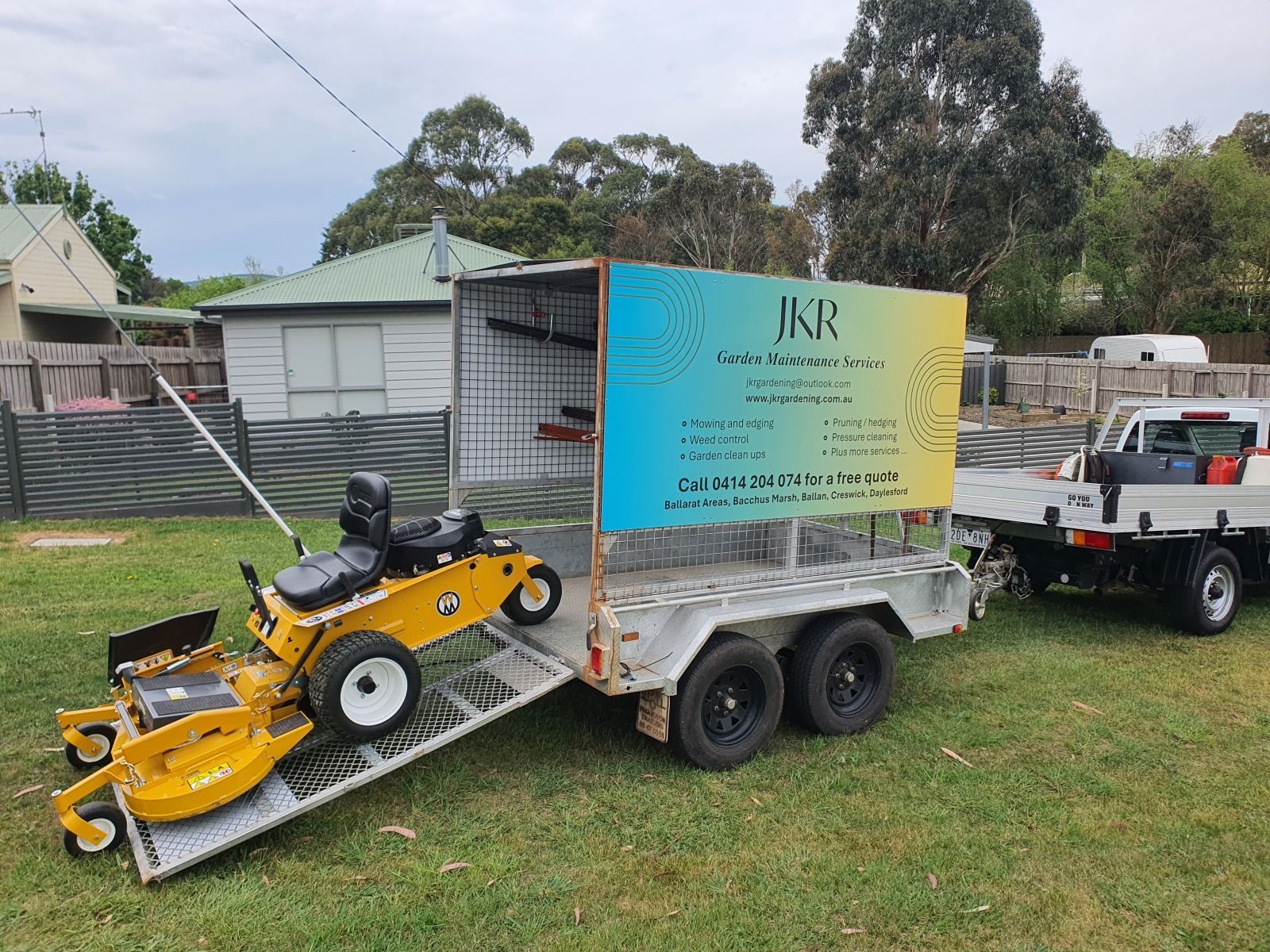 Yellow ride-on mower on a trailer with business signage, next to a white utility truck on grass — JKR Garden Maintenance Services in Ballan, VIC