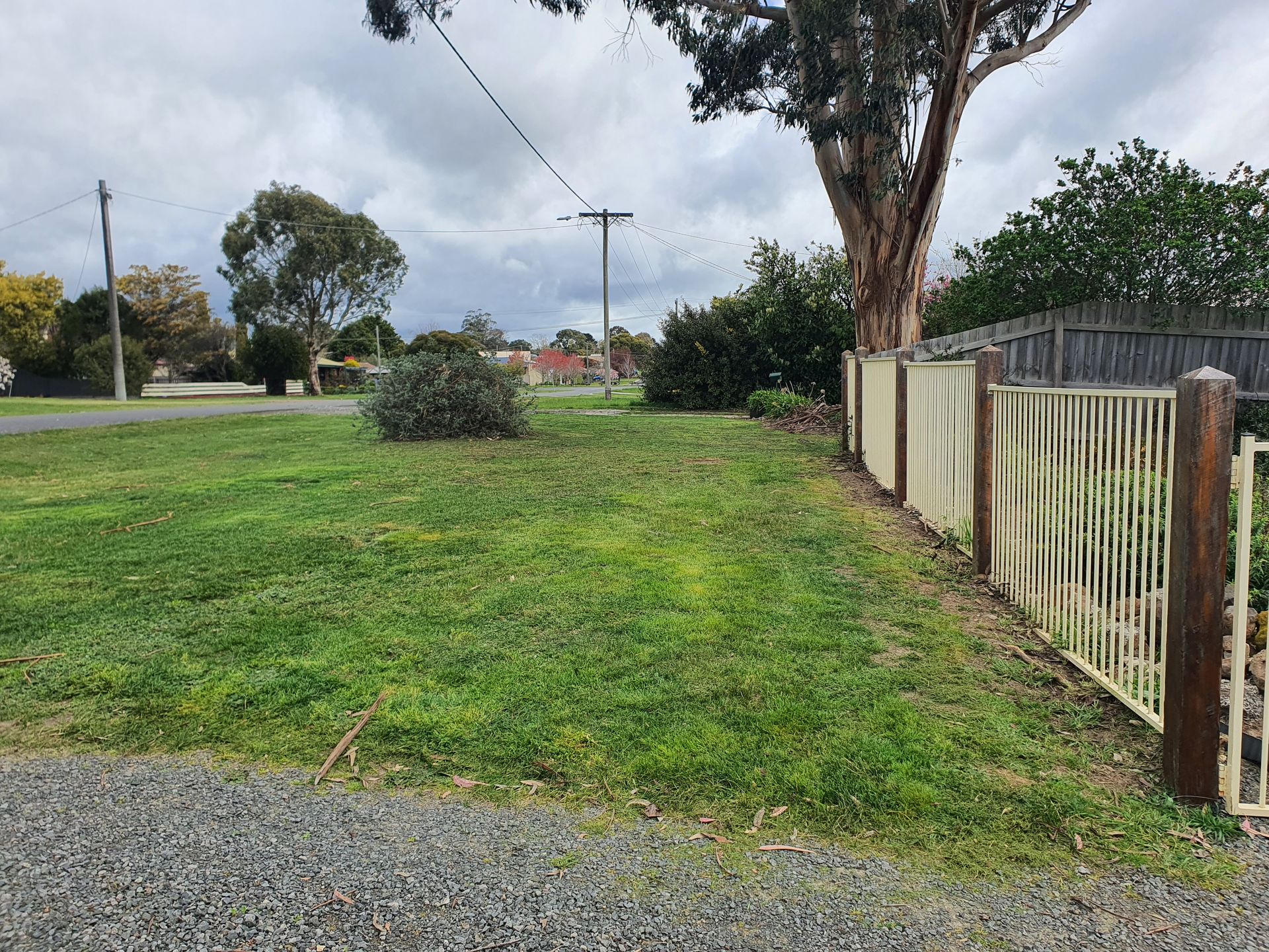 Grassy yard with a fence on the right, trees in the background, and a cloudy sky overhead — JKR Garden Maintenance Services in Ballan, VIC