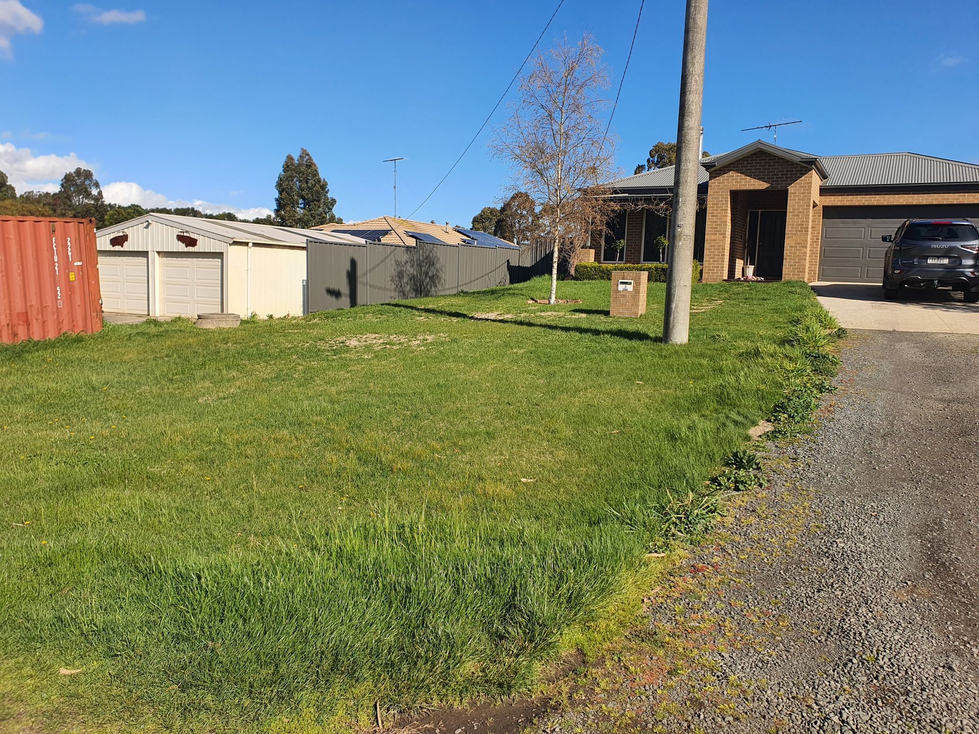 Grassy front yard of a house on a sunny day, with a red container on the left, and a parked car — JKR Garden Maintenance Services in Ballan, VIC